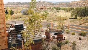 A patio with a grill, chairs, and a view of a hilly landscape.