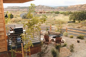 A patio with a grill, chairs, and a view of a hilly landscape.