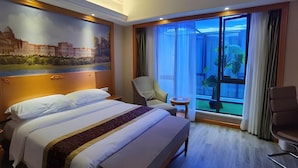 A hotel room with a large bed, a chair, a small table, and a large window with a view of a building and greenery. - Vienna Hotel Shanghai Yangpu Wujiaochang (Shanghai)
