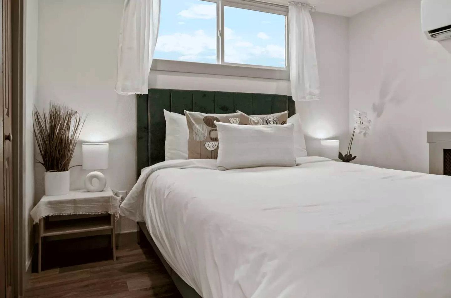 A bedroom with a bed, bedside table, lamp, and a window with curtains.