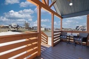Eine überdachte Terrasse mit Holzgeländer, einem Tisch und Stühlen sowie Blick auf Wohnmobile im Hintergrund.