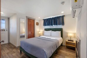 Ein Hotelzimmer mit Bett, Nachttischlampen, einer Tür, einem Fenster und einer Wand-Klimaanlage.
