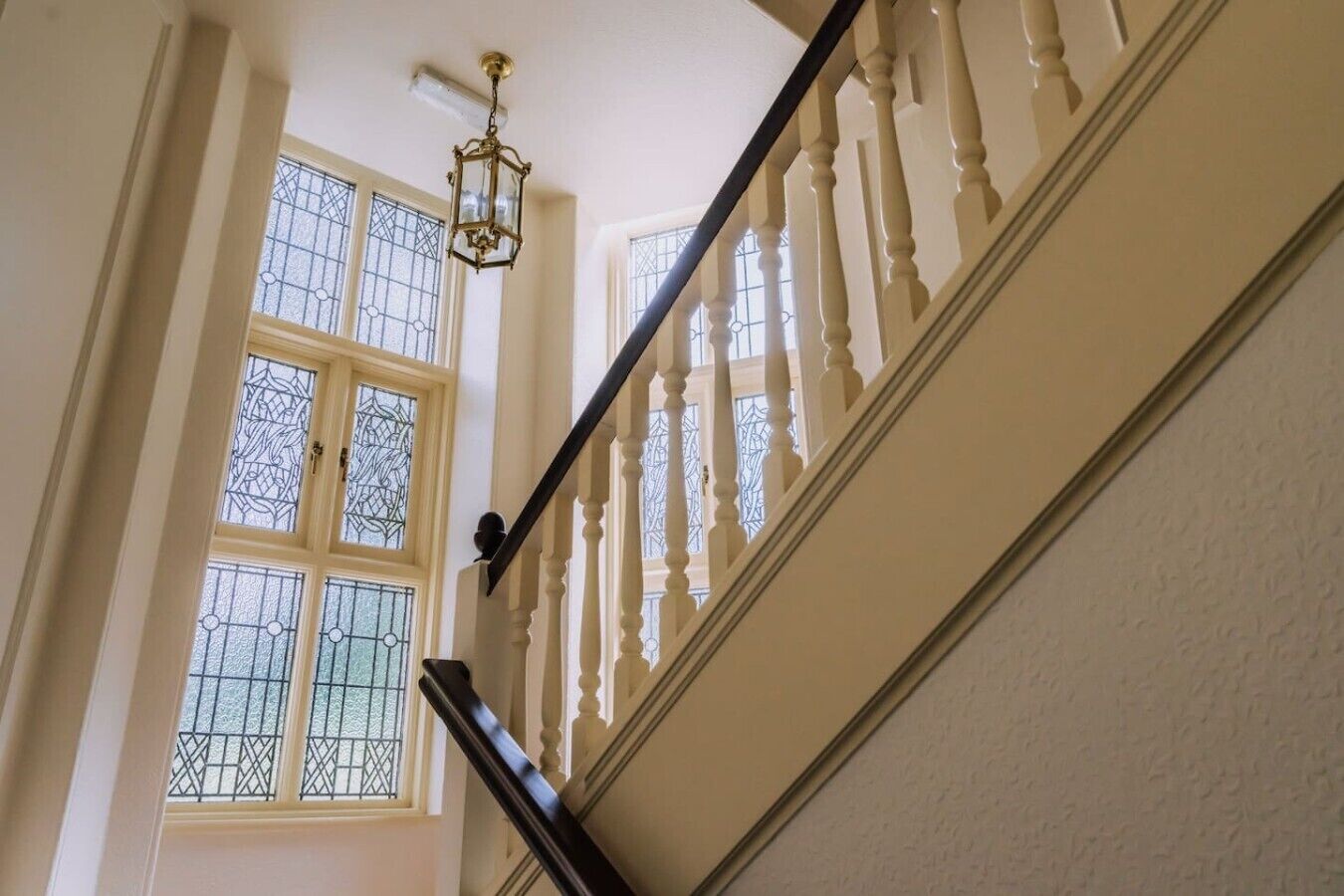 Een trap met een balustrade, een kroonluchter en een raam met decoratieve ijzeren tralies.