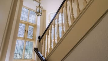 Een trap met een balustrade, een kroonluchter en een raam met decoratieve ijzeren tralies.