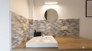 Ein Badezimmer mit einem rechteckigen Waschbecken, einem runden Spiegel und einer Wand mit geometrischem Muster.