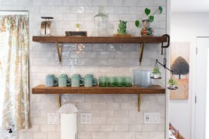 A kitchen with two wooden shelves holding mugs and glassware, a hanging plant, and a painting on the wall. - NEW Pup Friendly 3BR Country Home 10 mins to SLO (Santa Margarita)