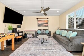 A living room with a flat-screen TV, ceiling fan, sofa, coffee table, and a foosball table. - NEW Pup Friendly 3BR Country Home 10 mins to SLO (Santa Margarita)