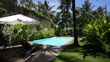 Una piscina con sillones de descanso y una sombrilla, rodeada de exuberante vegetación tropical.