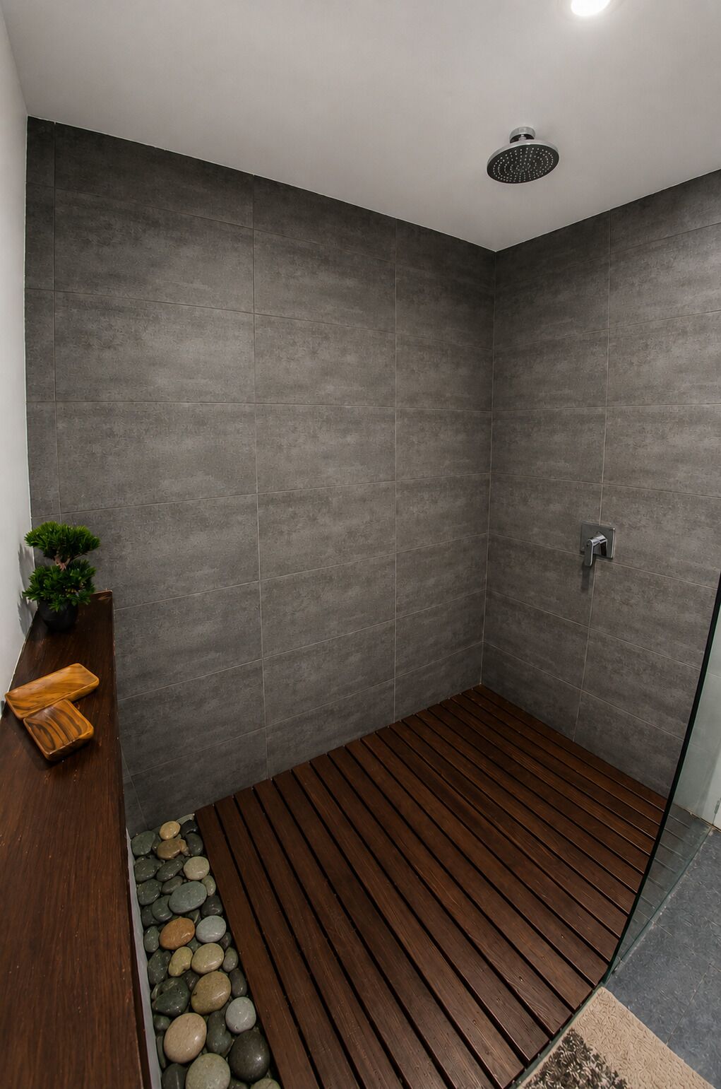 A modern shower with grey tiles, a wooden floor, and a small plant on a shelf.