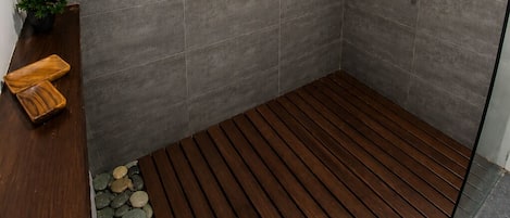 A modern shower with grey tiles, a wooden floor, and a small plant on a shelf.