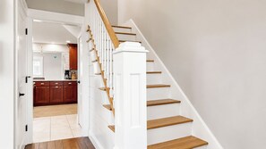 A staircase with white walls and wooden steps leading to a kitchen area. - Salt & Soul Retreat by Bayley Vacation Rentals (Old Orchard Beach)