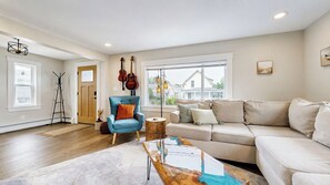 A living room with a blue armchair, beige sofa, and a coffee table with a painting. - Salt & Soul Retreat by Bayley Vacation Rentals (Old Orchard Beach)