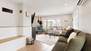 A living room with a sofa, a coffee table, and a blue armchair. There are guitars on the wall and a cabinet with books. - Salt & Soul Retreat by Bayley Vacation Rentals (Old Orchard Beach)