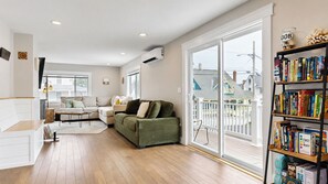 A spacious living room with a green sofa, a white couch, and a bookshelf filled with books. - Salt & Soul Retreat by Bayley Vacation Rentals (Old Orchard Beach)