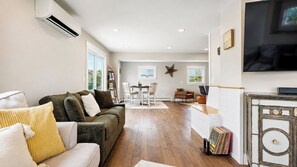 A living room with a sofa, a dining area with chairs, a fireplace, and a television mounted on the wall. - Salt & Soul Retreat by Bayley Vacation Rentals (Old Orchard Beach)