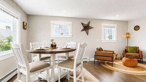 A dining area with a round table, white chairs, and a brown rug. - Salt & Soul Retreat by Bayley Vacation Rentals (Old Orchard Beach)