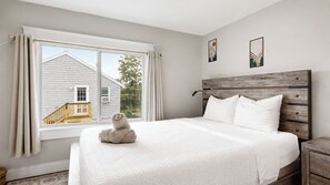 A bedroom with a large bed, a wooden headboard, and a window with curtains. - Salt & Soul Retreat by Bayley Vacation Rentals (Old Orchard Beach)