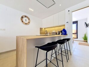 A modern kitchen with a wooden island, black bar stools, and a wall clock. - Private Roof Terrace & Pool View Penthouse (Mar de Cristal)