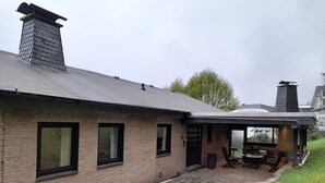 A brick house with a covered patio area, a chimney, and a view of a lake. - Holiday Home 'Am See' with Lake View, Private Terrace and Private Garden (Sundern)
