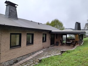 Ein Backsteinhaus mit überdachter Terrasse, einem Schornstein und Blick auf einen See.