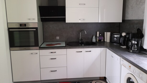 A compact kitchen with white cabinets, a built-in oven, a black range hood, a sink, and a coffee maker. - Holiday Home 'Am See' with Lake View, Private Terrace and Private Garden (Sundern)