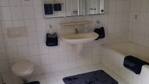 A bathroom with a toilet, sink, and bathtub. There are two black rugs on the floor. - Holiday Home 'Am See' with Lake View, Private Terrace and Private Garden (Sundern)