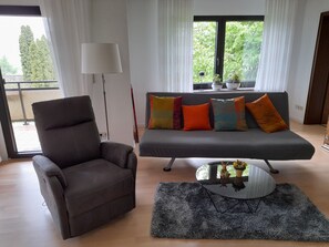 A modern living room with a grey sofa, a brown armchair, a glass coffee table, and a grey rug.
