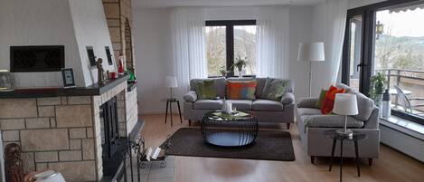 A modern living room with a fireplace, a sofa set, a coffee table, and large windows offering a view.