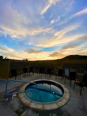 Un bain à remous doté d’une rambarde en métal, entouré de chaises, avec en arrière-plan un ciel au coucher du soleil.
