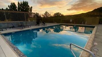 A swimming pool with a metal safety railing, surrounded by a concrete deck with lounge chairs.
