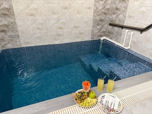 A spa area with a blue-tiled hot tub, a tray with fruits and drinks, and a towel rack.