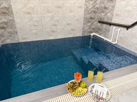 Un área de spa con un jacuzzi azulado, una bandeja con frutas y bebidas, y un perchero para toallas.
