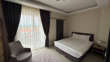 A hotel room with a bed, a chair, a nightstand, a lamp, and a view of the outside.