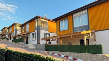 Une rangée de maisons modernes à deux étages, dotées de balcons, d’un chemin piétonnier pavé et d’un mur en pierre.