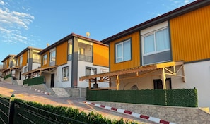 A row of modern two-story houses with balconies, a paved walkway, and a stone wall.