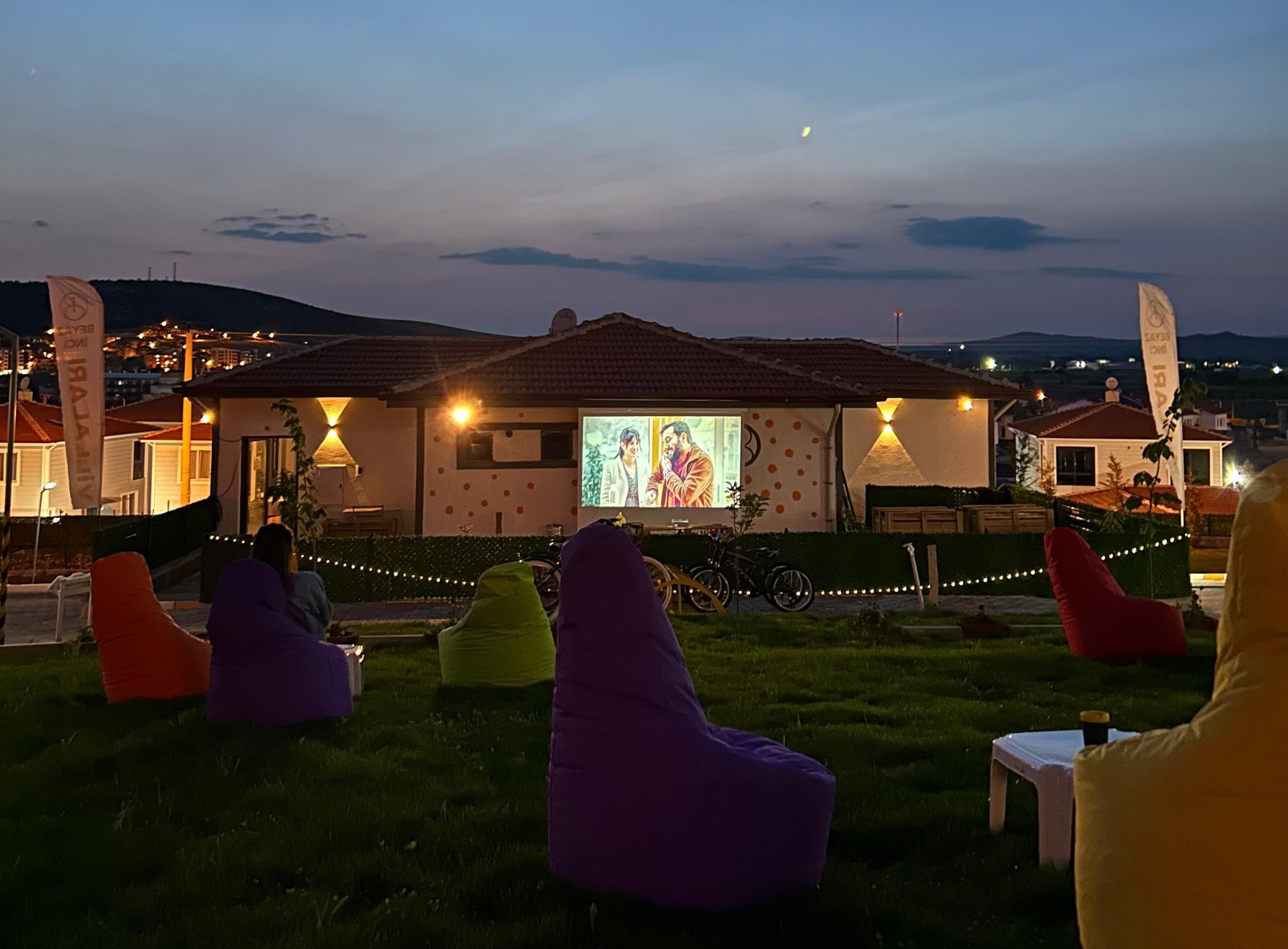 A building with a projection screen displaying a movie, outdoor seating with bean bags, and a bicycle parked in front.