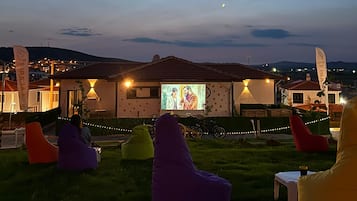A building with a projection screen displaying a movie, outdoor seating with bean bags, and a bicycle parked in front.