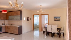 A modern kitchen with a dining area, a chandelier, and a view through a doorway. - Albania Dream Saranda Apartment (Sarandë)