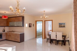 A modern kitchen with a dining area, a chandelier, and a view through a doorway. - Albania Dream Saranda Apartment (Sarandë)