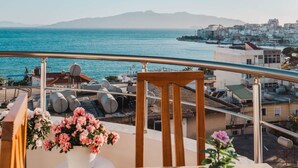 A balcony with a view of the sea and buildings, a wooden table, and a potted plant. - Albania Dream Saranda Apartment (Sarandë)