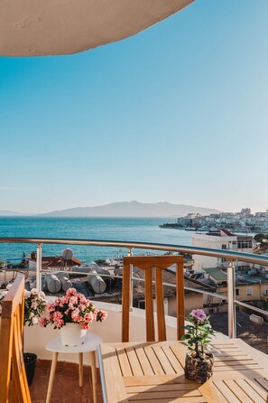 A balcony with a view of the sea and buildings, a wooden table, and a potted plant. - Albania Dream Saranda Apartment (Sarandë)