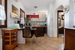 A compact kitchen with a microwave, stove, and red cabinets. There is a dining area with two chairs and a small table.