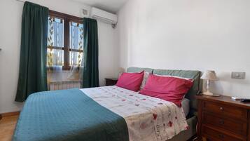 A bedroom with a bed, a bedside table, a lamp, and a window with curtains.