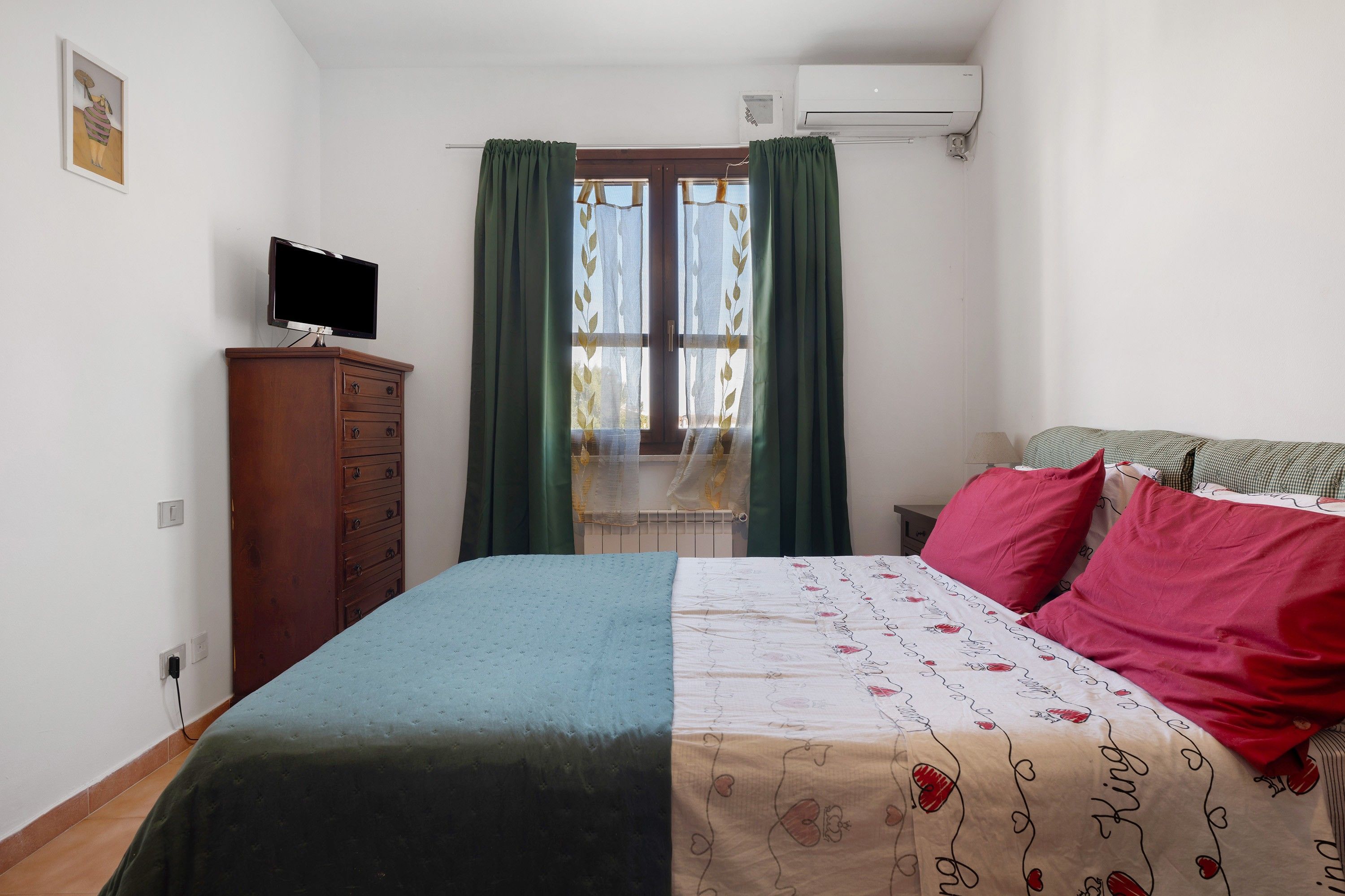 A bedroom with a bed, a dresser, a television, and a window with curtains.