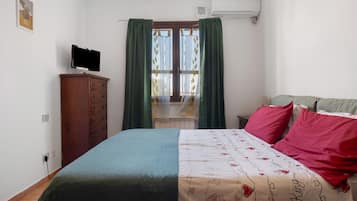 A bedroom with a bed, a dresser, a television, and a window with curtains.