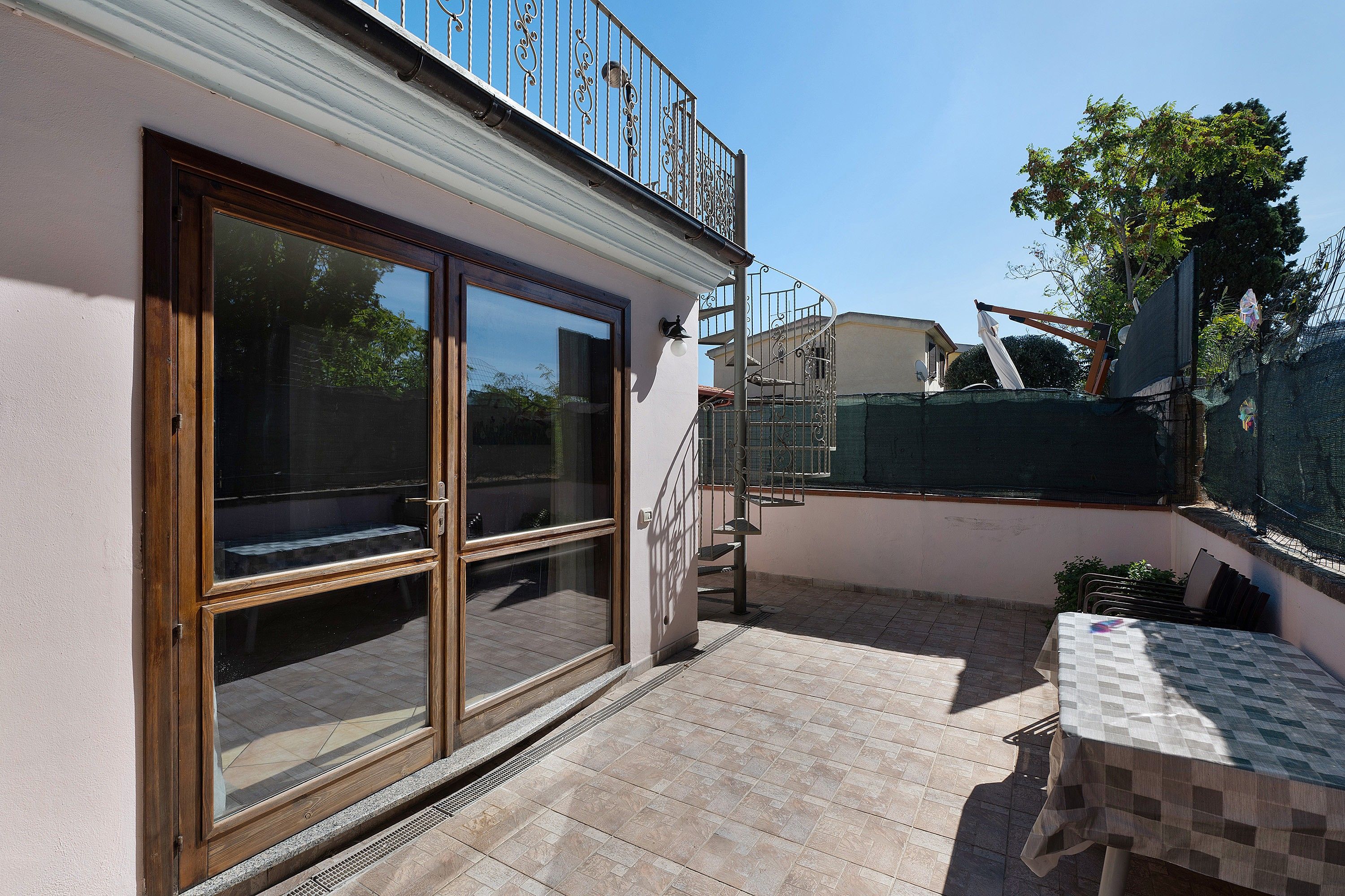Un immeuble résidentiel doté d’une entrée avec une porte-fenêtre coulissante, d’un petit patio extérieur avec une table et d’un escalier en métal menant à un étage supérieur.
