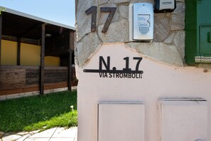 A building corner with a stone wall, a metal number '17', a white sign with 'N.17 VIA STROMBOLI', and a green door.