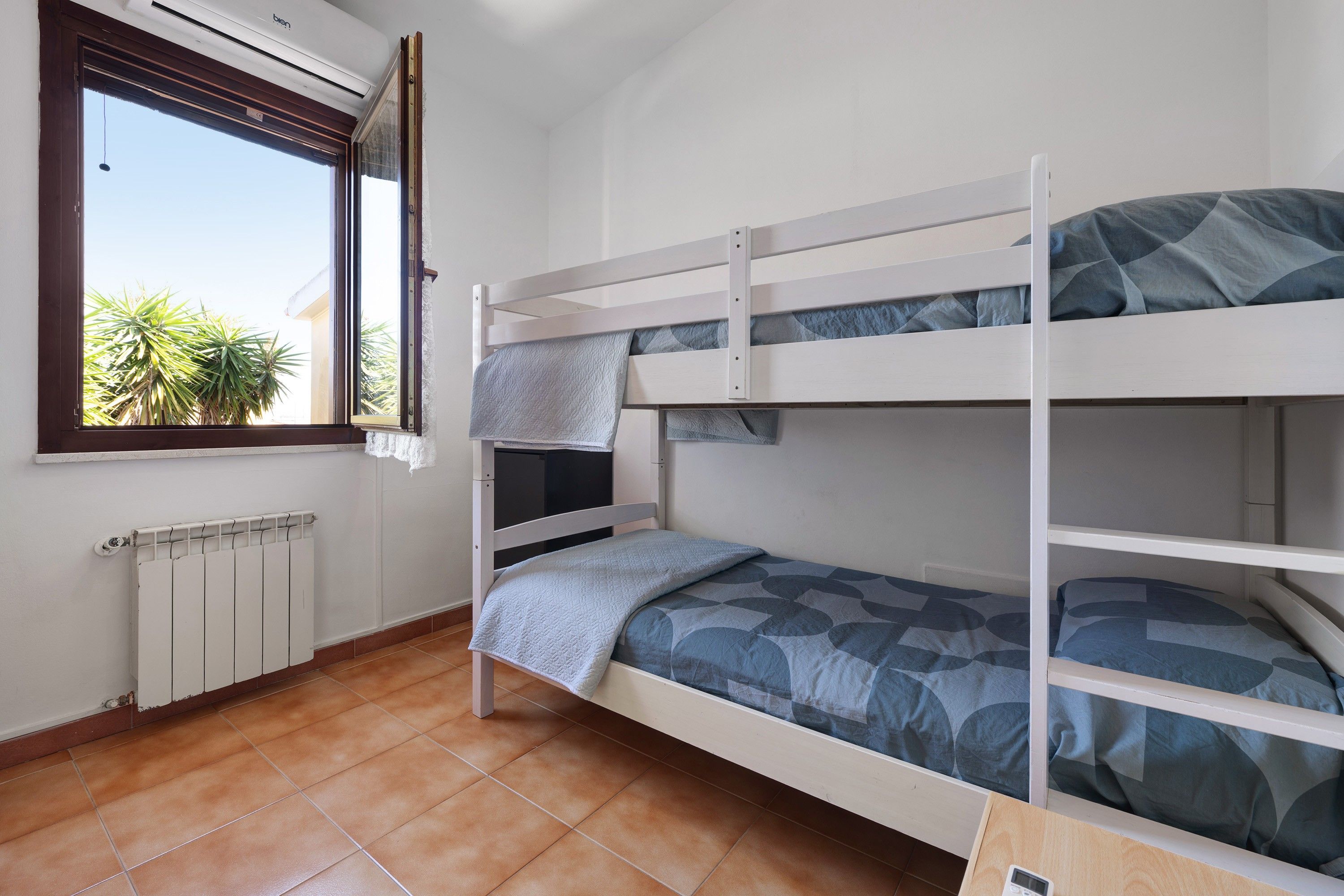 Ein Schlafraum mit Etagenbett, Fenster, Heizkörper und Fliesenboden.