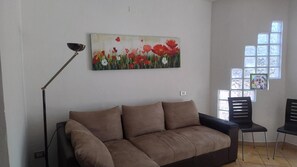 Un soggiorno con un divano marrone, una lampada da terra e un quadro con fiori rossi al muro.