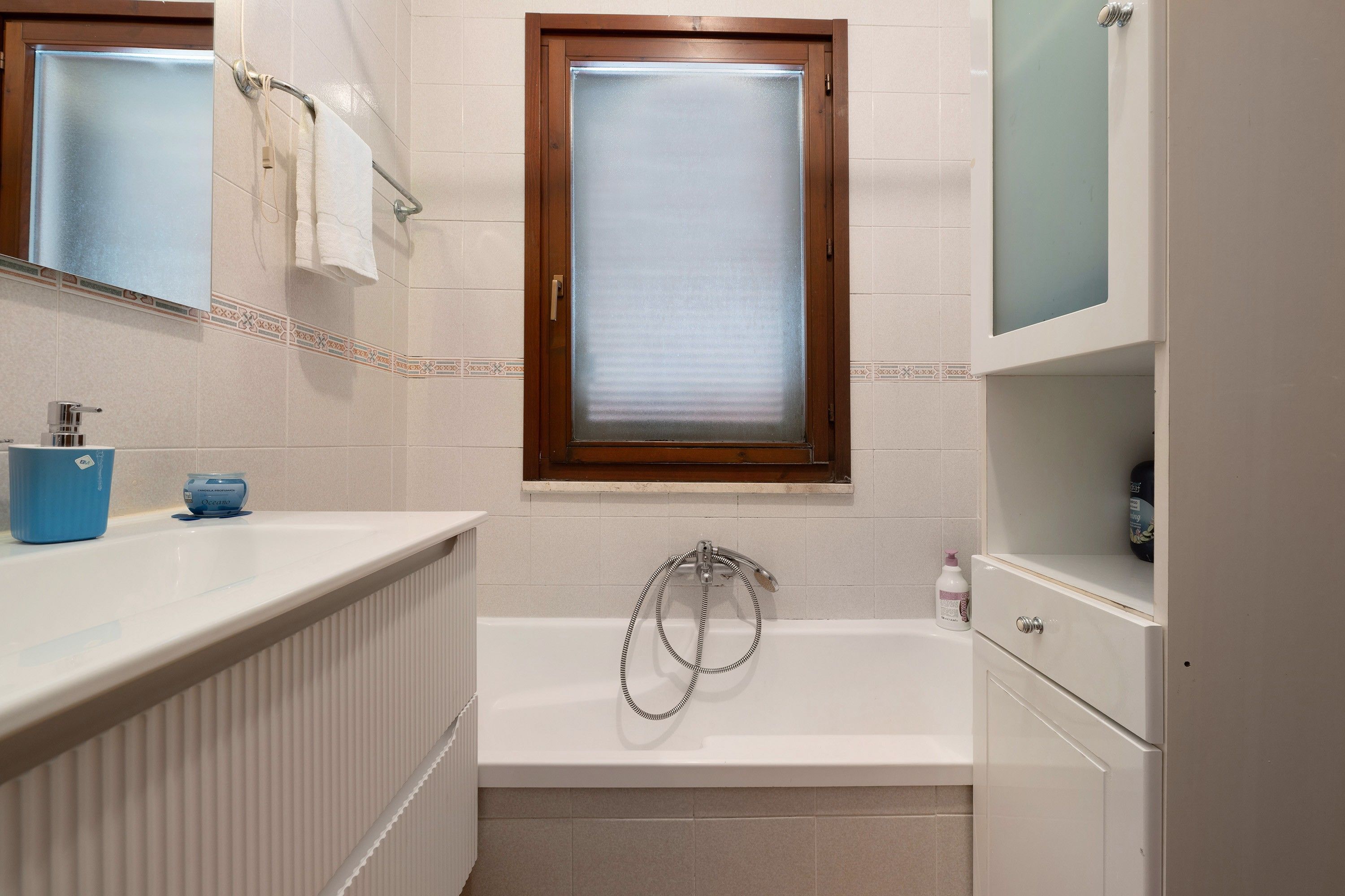 A bathroom with a bathtub, a towel rack, a window, and a shelf with toiletries.